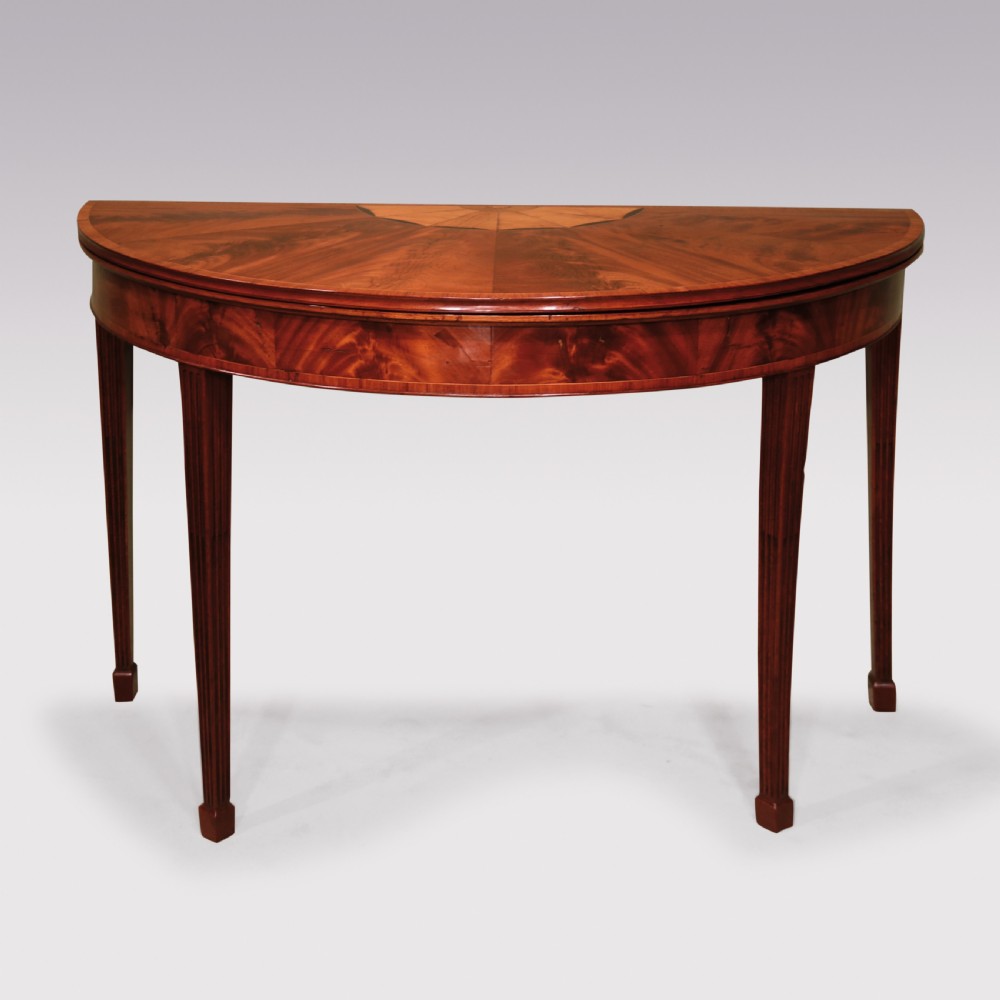 A late eighteenth-century semi-circular mahogany fold-over card table featuring fan-segmented veneer inlay on the top and fluted tapered legs.