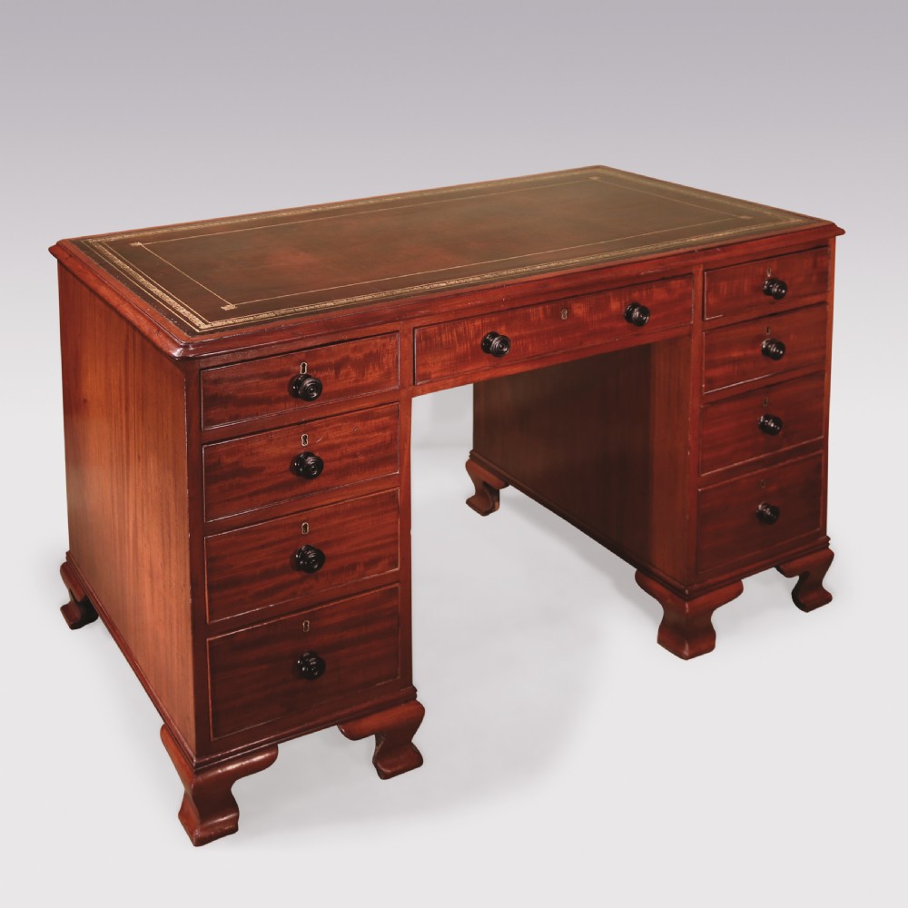 A compact George III mahogany pedestal desk featuring a dark leather writing inset surface, multiple small drawers with turned knobs, and shaped feet.