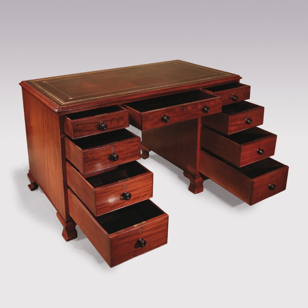 A compact George III mahogany pedestal desk featuring a dark leather writing inset surface, multiple small drawers with turned knobs, and shaped feet. View II