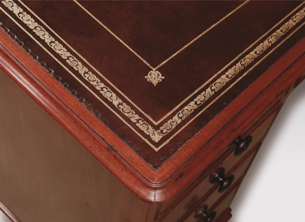 A compact George III mahogany pedestal desk featuring a dark leather writing inset surface, multiple small drawers with turned knobs, and shaped feet. View IV