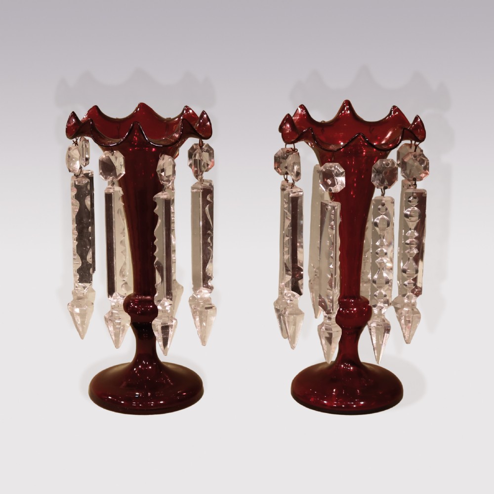 A pair of mid-19th century deep red cranberry glass mantle lustres with frilled rims and hanging clear cut-crystal prisms on circular bases.