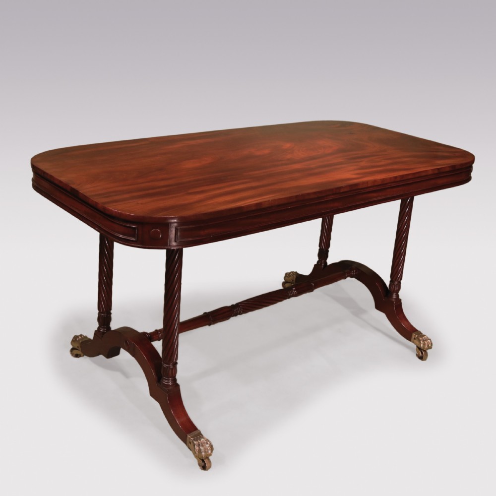 A dark mahogany Regency writing table featuring a rectangular top with rounded corners, spiral-turned end supports, a low stretcher, and brass paw castors.