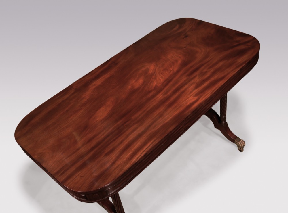 A dark mahogany Regency writing table featuring a rectangular top with rounded corners, spiral-turned end supports, a low stretcher, and brass paw castors. View III