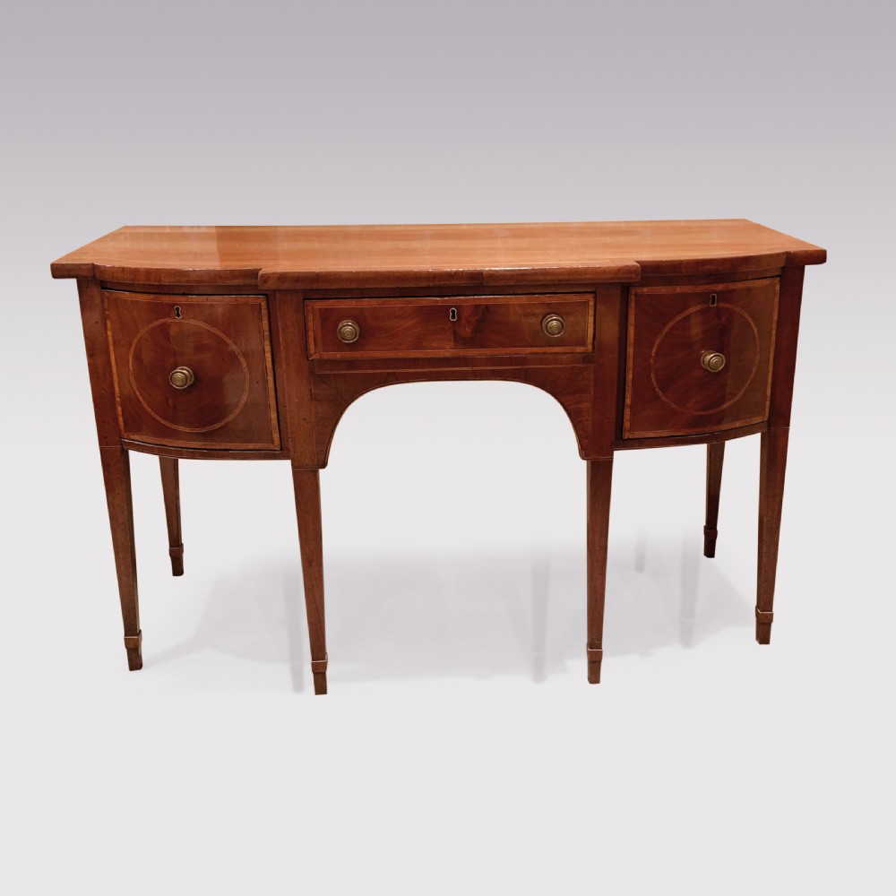 An eighteenth-century Sheraton mahogany sideboard featuring a central drawer flanked by circular inlaid cupboards, supported on slender tapered legs.