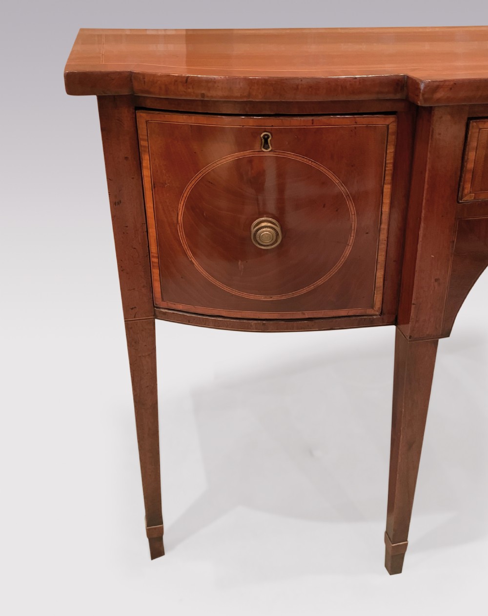 An eighteenth-century Sheraton mahogany sideboard featuring a central drawer flanked by circular inlaid cupboards, supported on slender tapered legs. View V