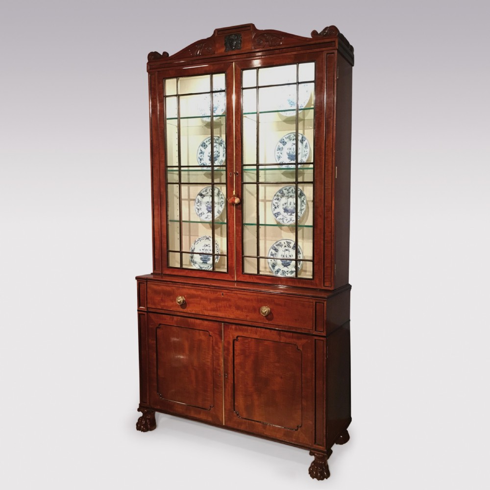 A Regency period mahogany secretaire bookcase featuring glazed upper doors displaying ceramics, a carved mask pediment, and carved lion paw feet. View II