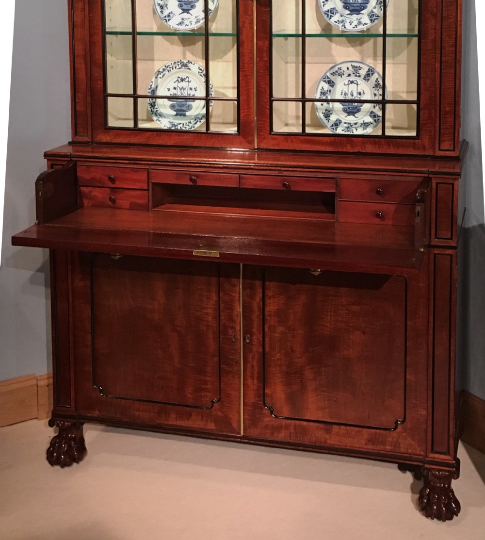 A Regency period mahogany secretaire bookcase featuring glazed upper doors displaying ceramics, a carved mask pediment, and carved lion paw feet. View III