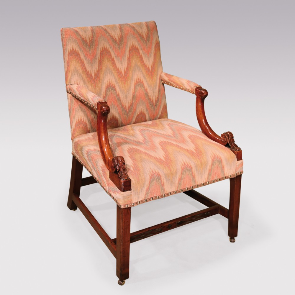 An 18th-century mahogany Gainsborough armchair featuring patterned flame stitch upholstery, carved armrests, and square legs with brass castors.