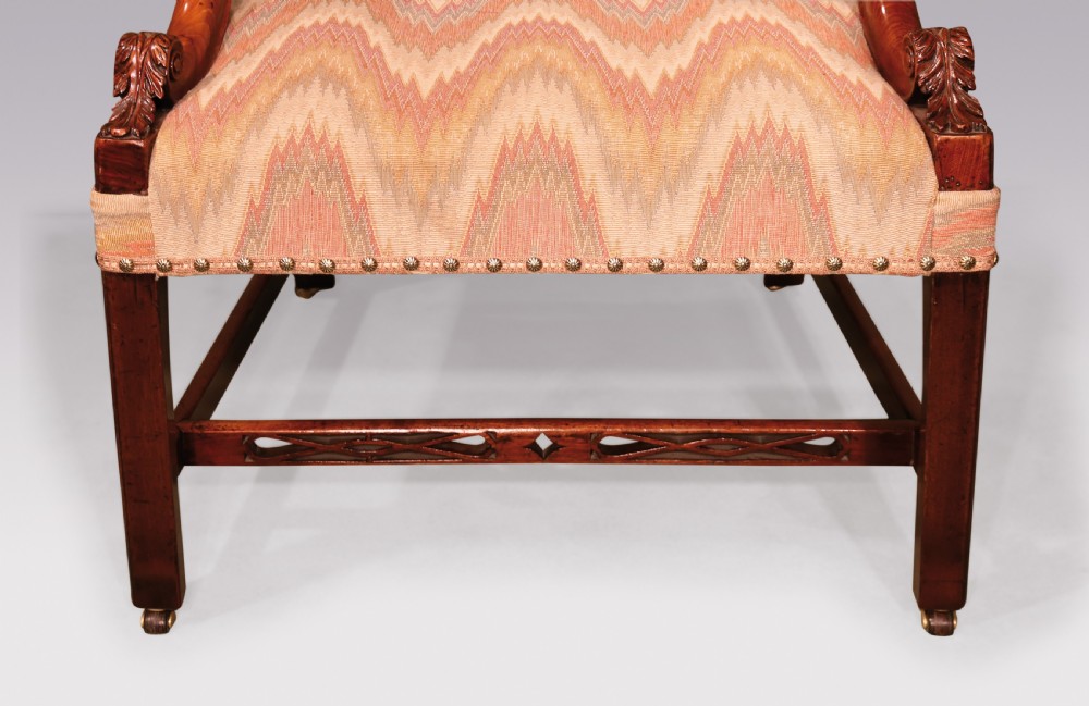 An 18th-century mahogany Gainsborough armchair featuring patterned flame stitch upholstery, carved armrests, and square legs with brass castors. View II