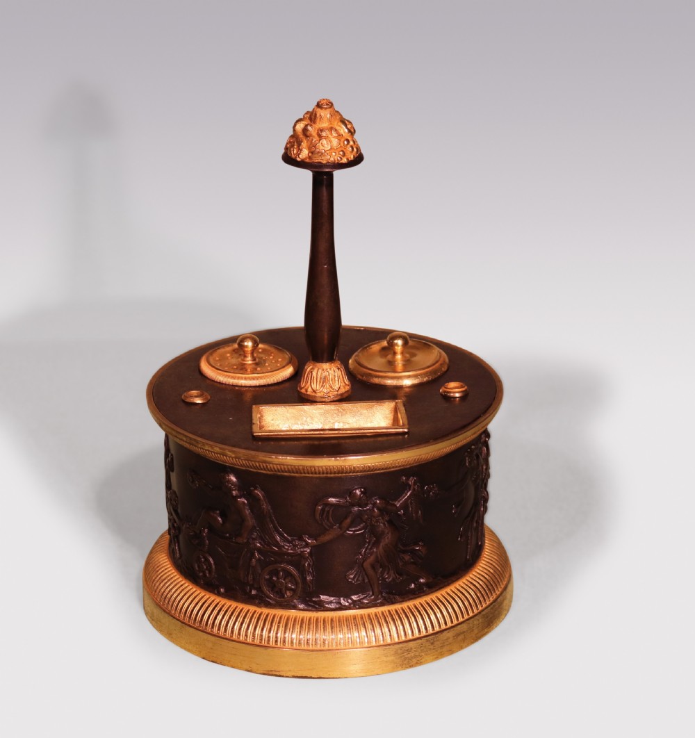 A 19th-century cylindrical French patinated bronze encrier featuring a classical relief frieze, gilded bronze borders, inkwell lids, and a central column handle.