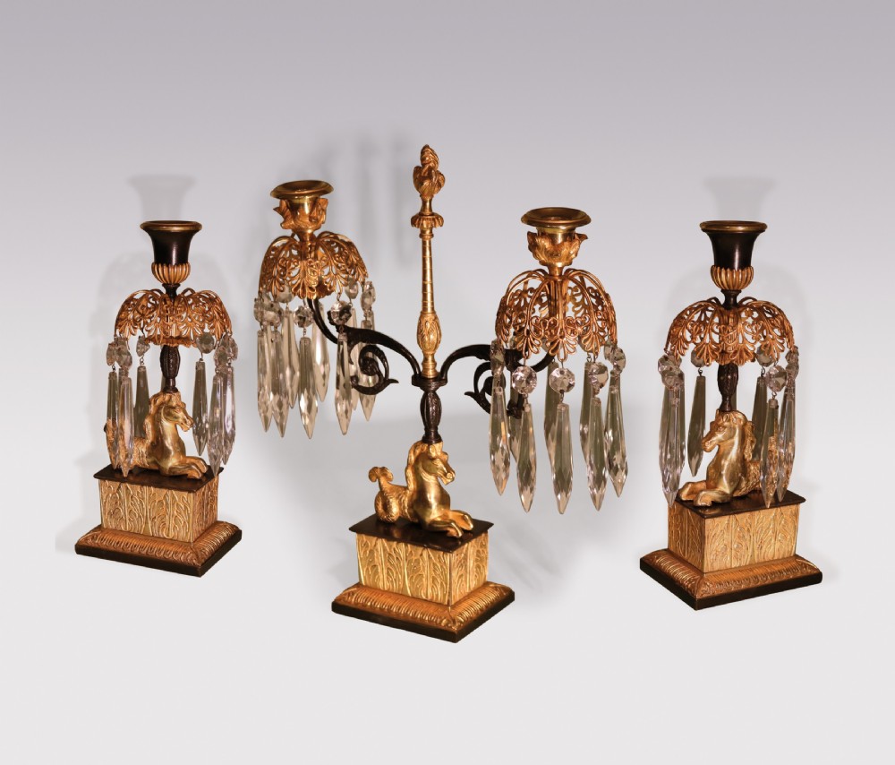 A set of three early 19th-century gilt bronze and patinated metal candlesticks featuring mythical seahorse mounts and hanging cut crystal drops.