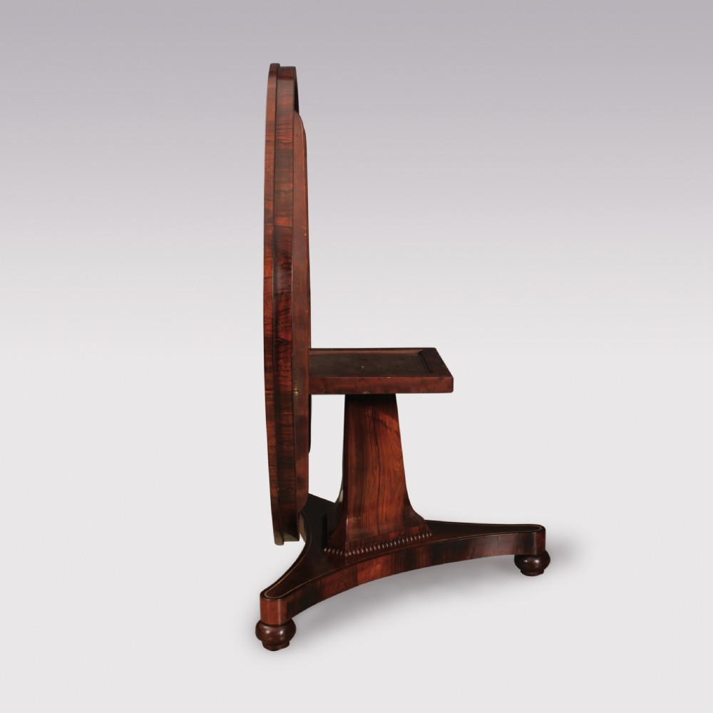 A circular Regency rosewood centre table featuring decorative brass inlay around the perimeter and supported by a pedestal on a triform base. View IV