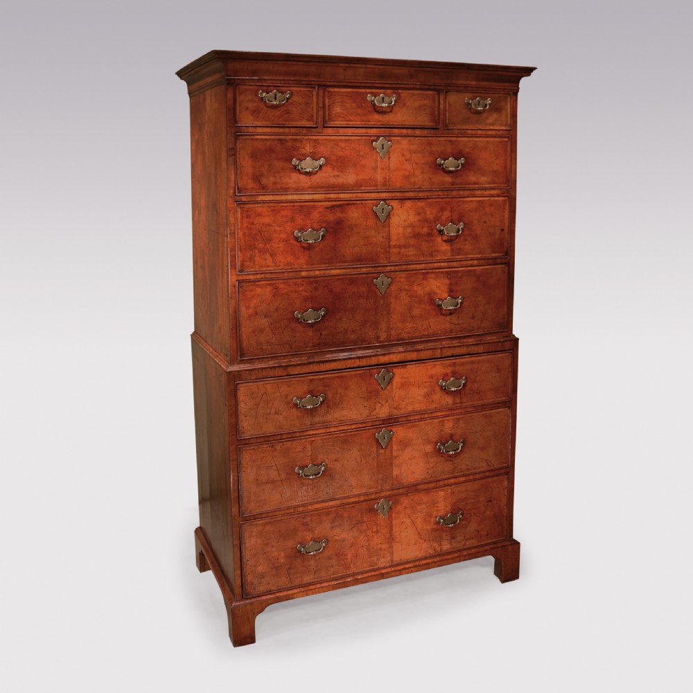 An 18th-century walnut chest on chest with two separate drawer sections, figured walnut veneers, bracket feet, and brass swing handles.