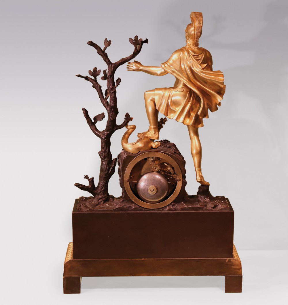 An early 19th-century French Empire clock crafted from gilt and patinated bronze, featuring a classical warrior figure standing beside a tree with a serpent atop a rectangular plinth. View IV
