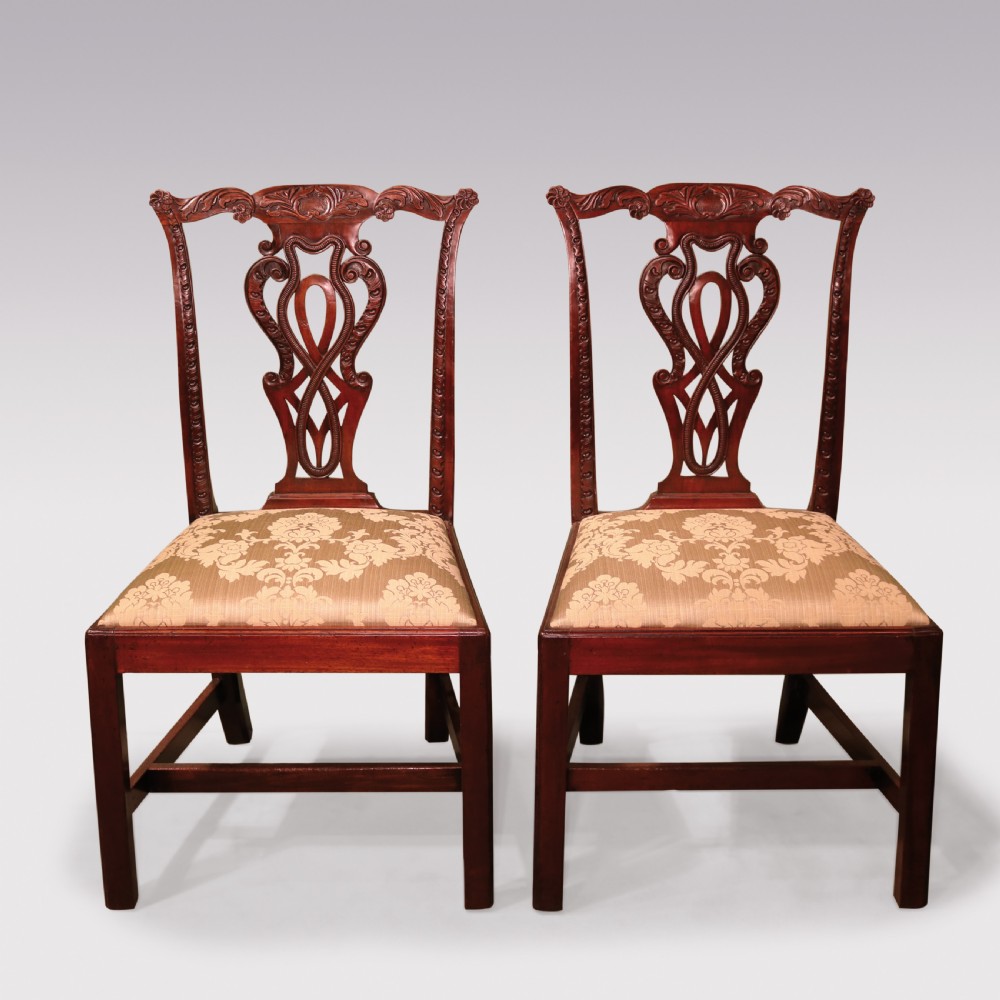 A pair of Georgian Chippendale carved mahogany single dining chairs featuring detailed pierced splats and patterned fabric upholstered seats.
