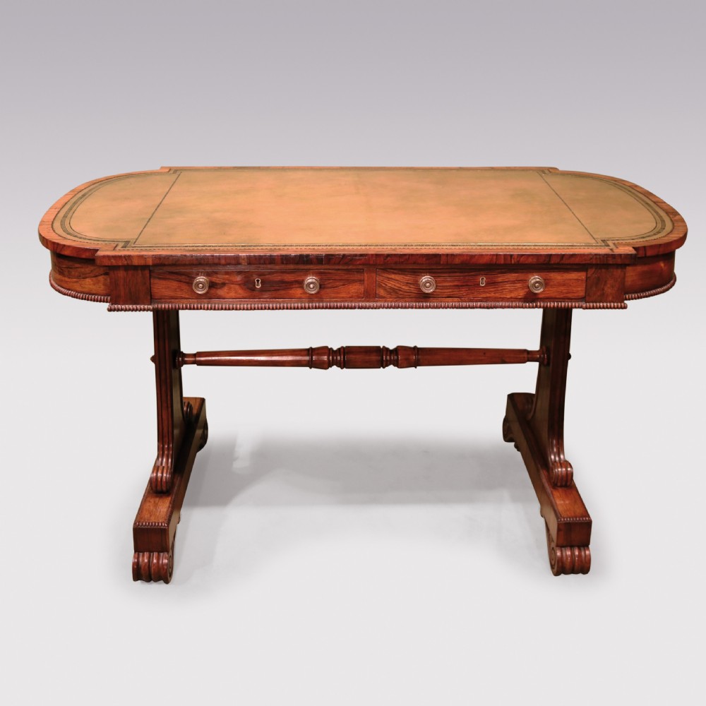 An early 19th-century Regency rosewood writing table featuring a green leather-inset top, two frieze drawers with brass handles, and trestle-end supports connected by a turned stretcher.