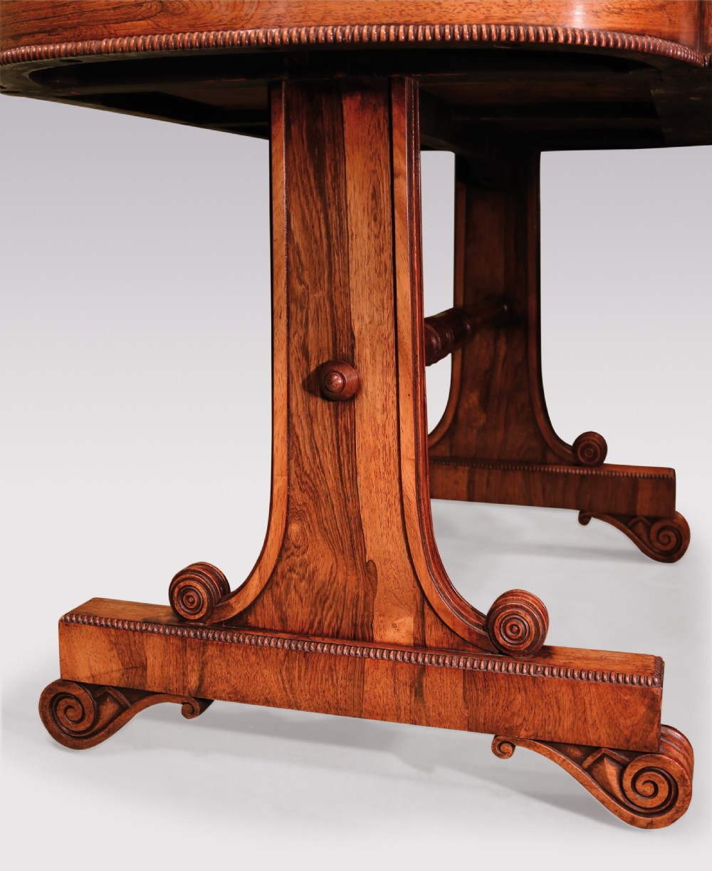An early 19th-century Regency rosewood writing table featuring a green leather-inset top, two frieze drawers with brass handles, and trestle-end supports connected by a turned stretcher. View VI