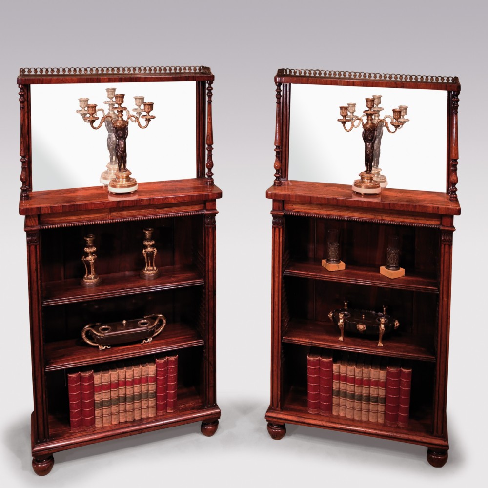 A pair of Regency period rosewood open bookcases featuring upper mirrored backs with brass gallery tops and turned support columns above open adjustable shelves.
