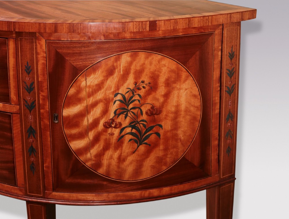 A late 18th-century Sheraton period demilune commode crafted from satinwood with floral marquetry panels and tapered legs. View V
