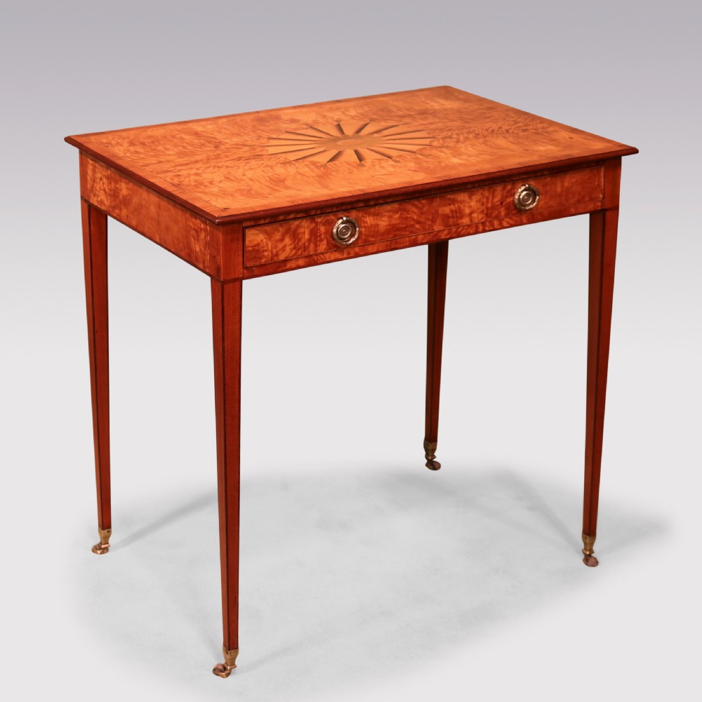 A late 18th-century Sheraton period satinwood side table featuring a starburst marquetry top, single drawer with ring pull handles, and square tapered legs on brass castors.