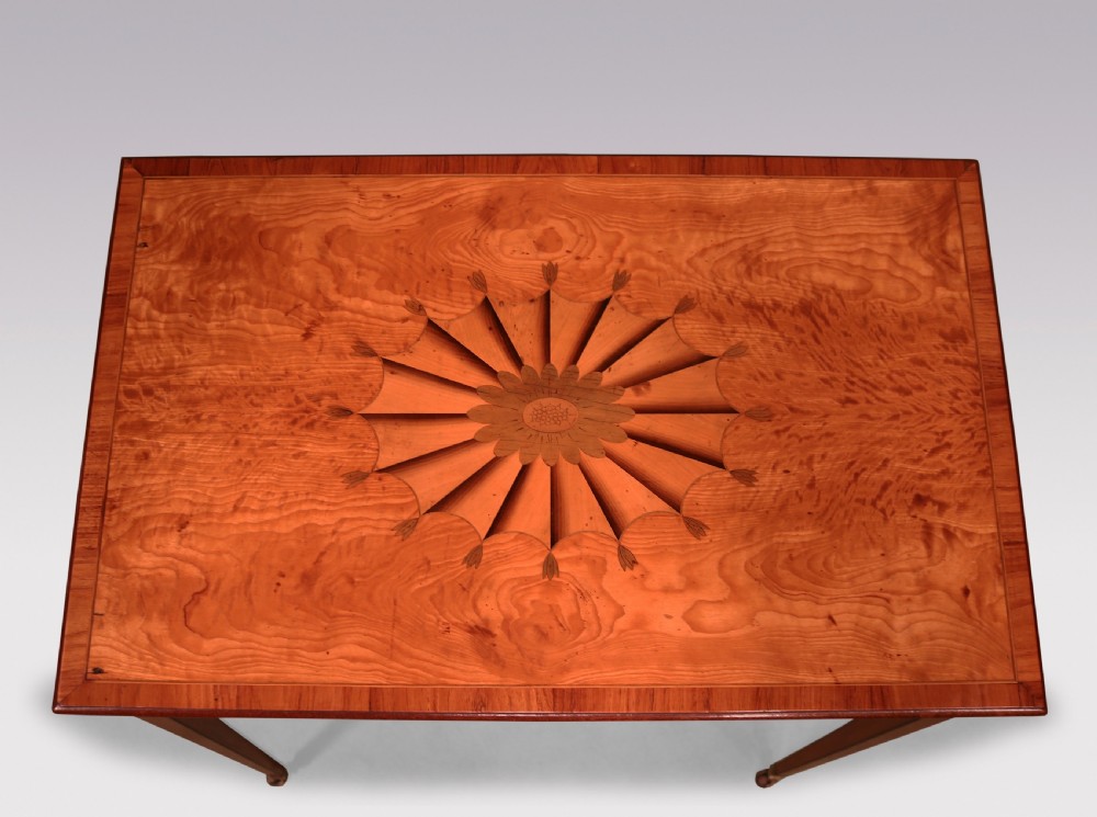 A late 18th-century Sheraton period satinwood side table featuring a starburst marquetry top, single drawer with ring pull handles, and square tapered legs on brass castors. View III