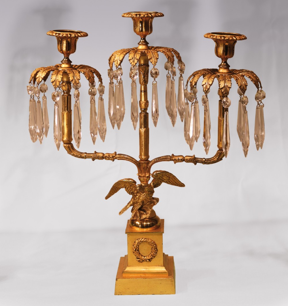 A three-piece Regency period ormolu and gilt bronze candelabra set featuring eagle bases, palm leaf tops, and hanging crystal drops. View II