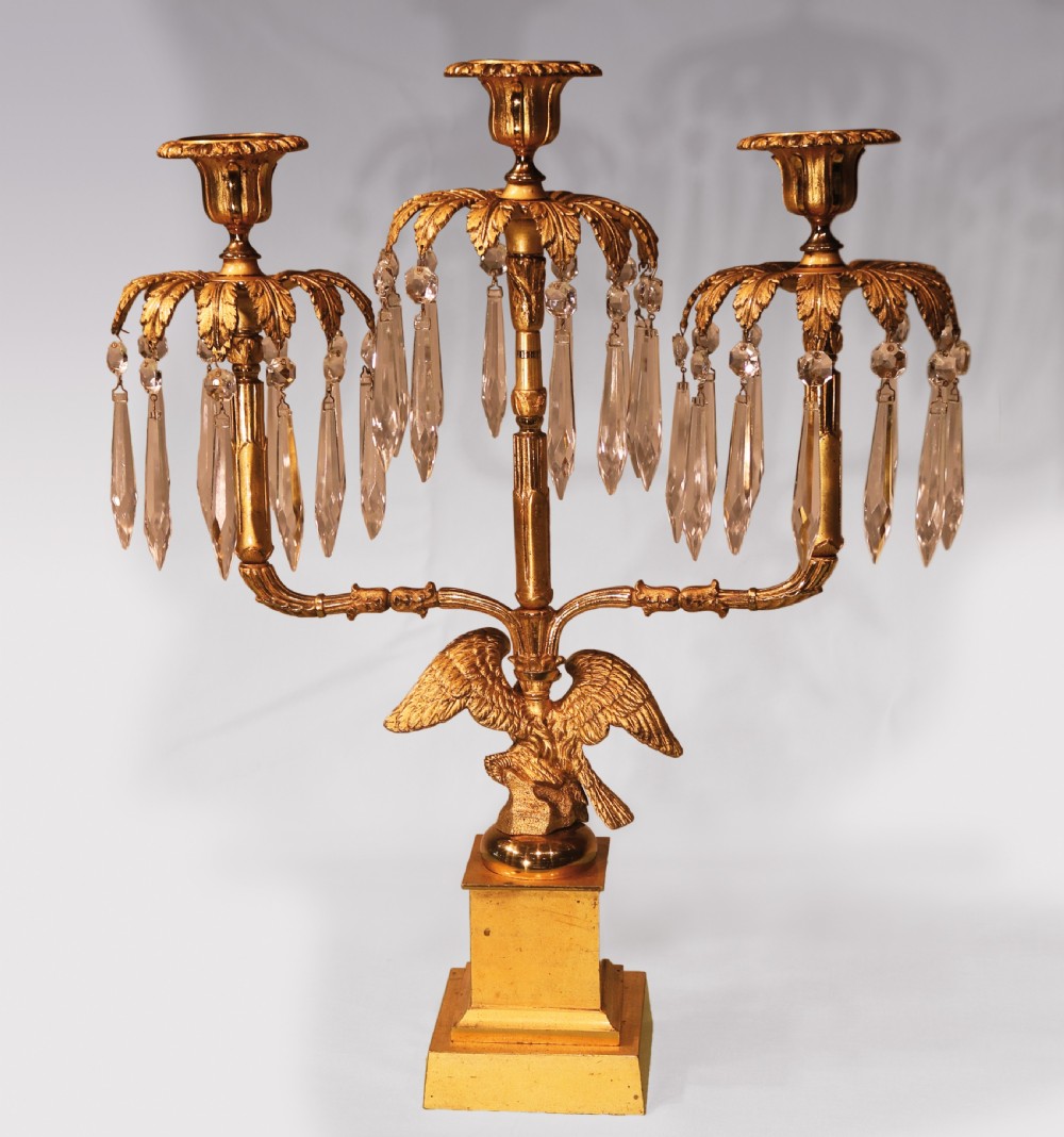 A three-piece Regency period ormolu and gilt bronze candelabra set featuring eagle bases, palm leaf tops, and hanging crystal drops. View IV