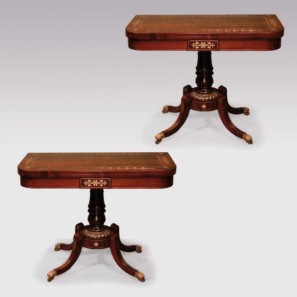 A pair of Regency period rosewood card tables featuring brass inlaid tops, turned central pedestals, and four splayed legs with brass paw feet.