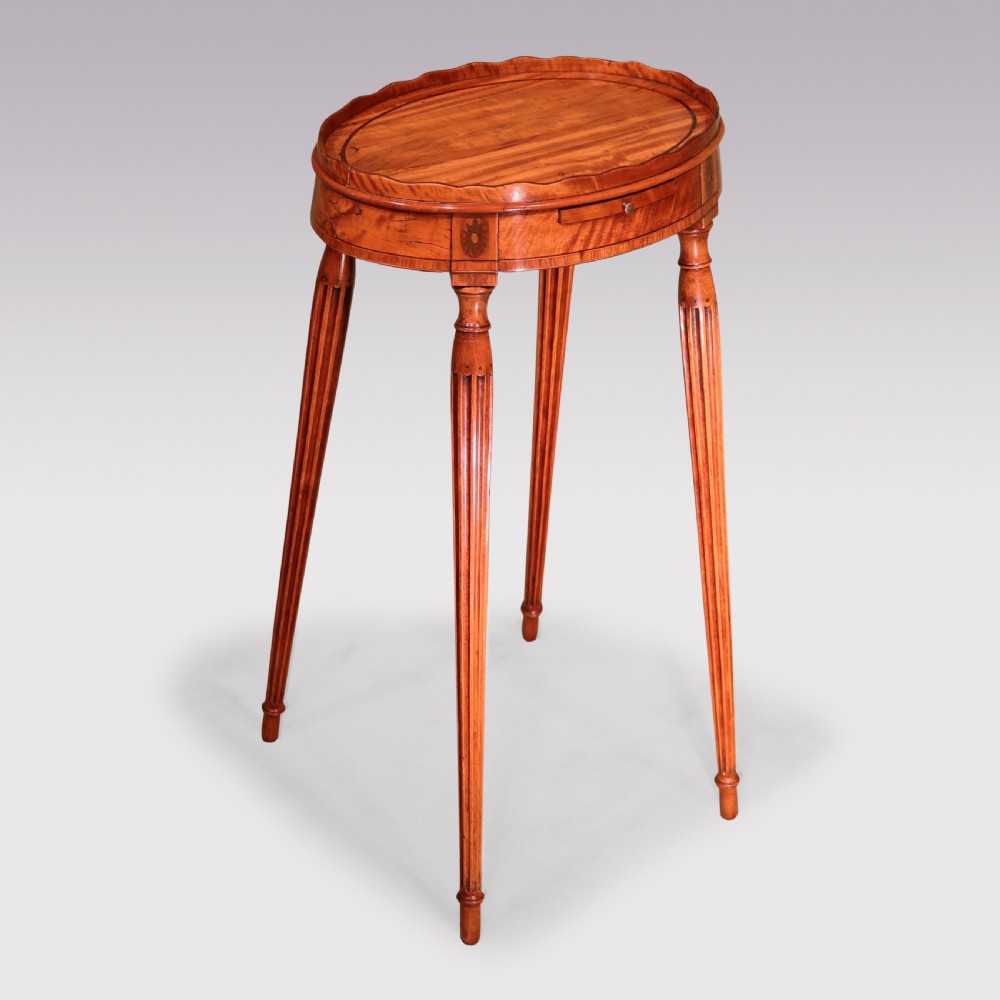A George III oval satinwood kettle stand featuring a scalloped gallery rim, fluted tapered legs, and an inlaid apron with a pull-out slide.