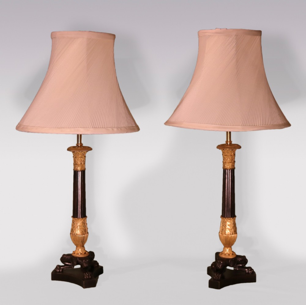 A pair of patinated bronze and gilt ormolu candlestick table lamps with fluted shafts, lion paw bases, and flared pleated fabric shades.