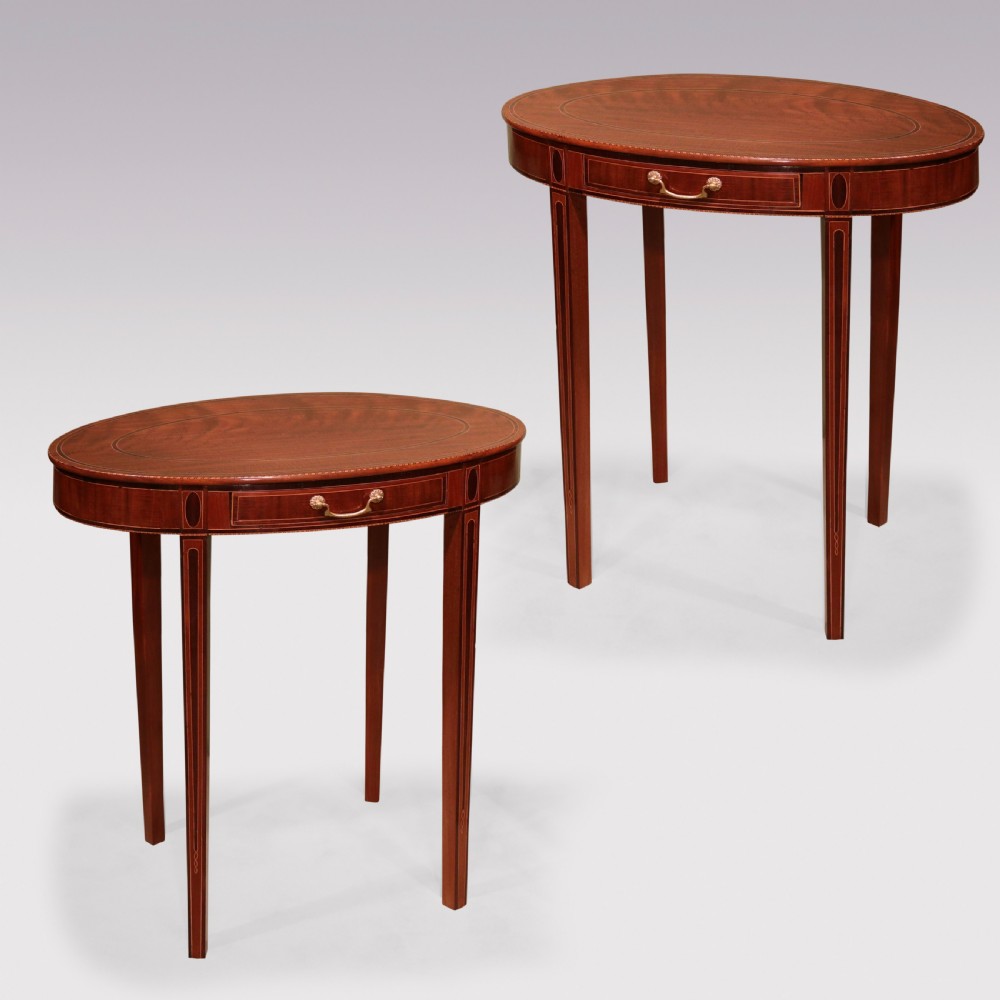 A pair of late 18th-century mahogany oval occasional tables featuring satinwood stringing, single frieze drawers with brass handles, and square tapered legs.
