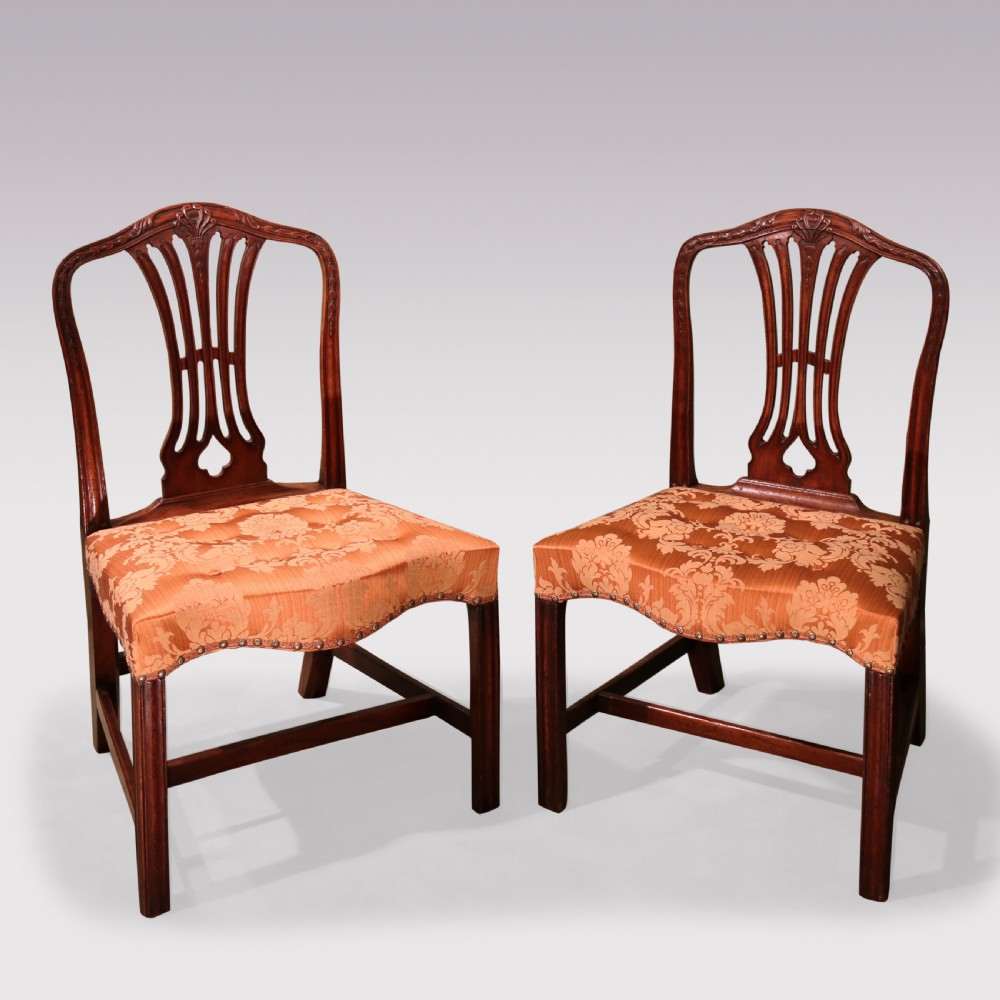 A pair of 18th-century Hepplewhite mahogany side chairs featuring pierced splat backs, serpentine seats upholstered in patterned terracotta damask, and square legs with H-stretchers.