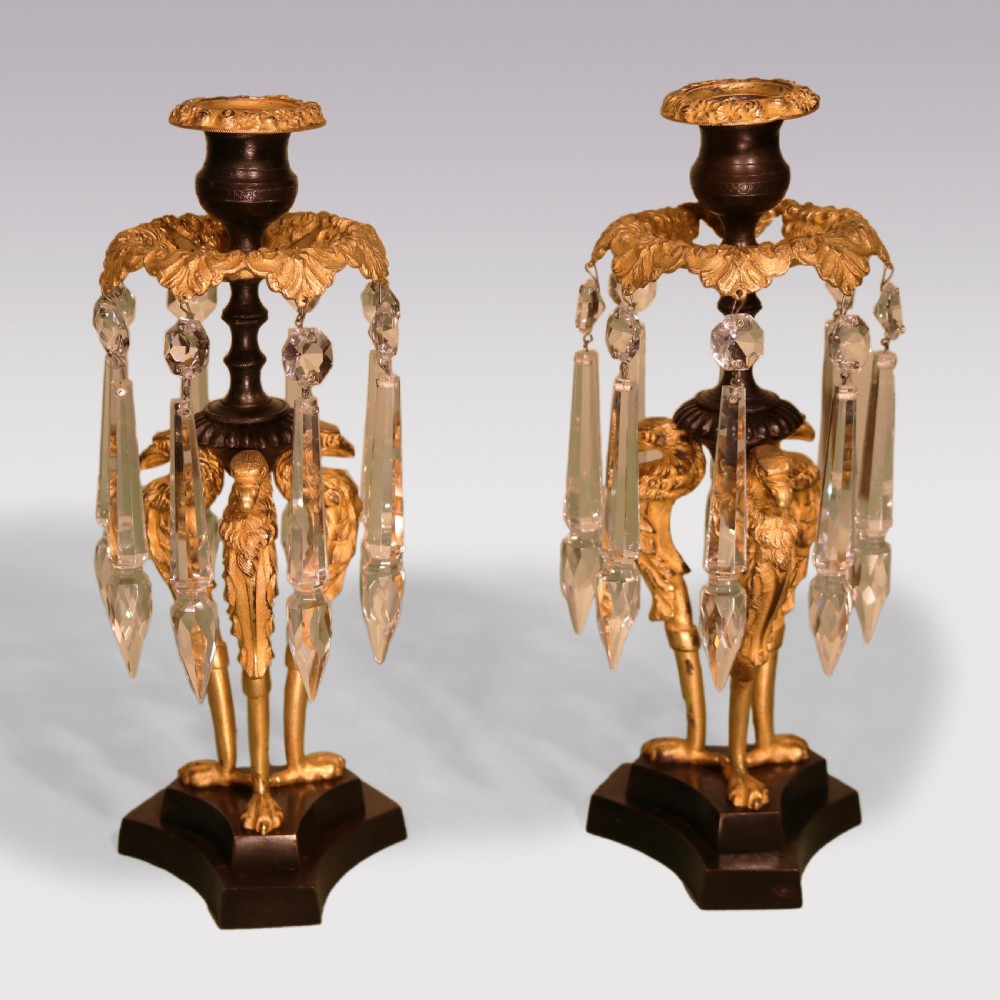 A pair of Regency period patinated bronze and gilt-bronze candle lustres with griffin supports and clear glass crystal droplets.