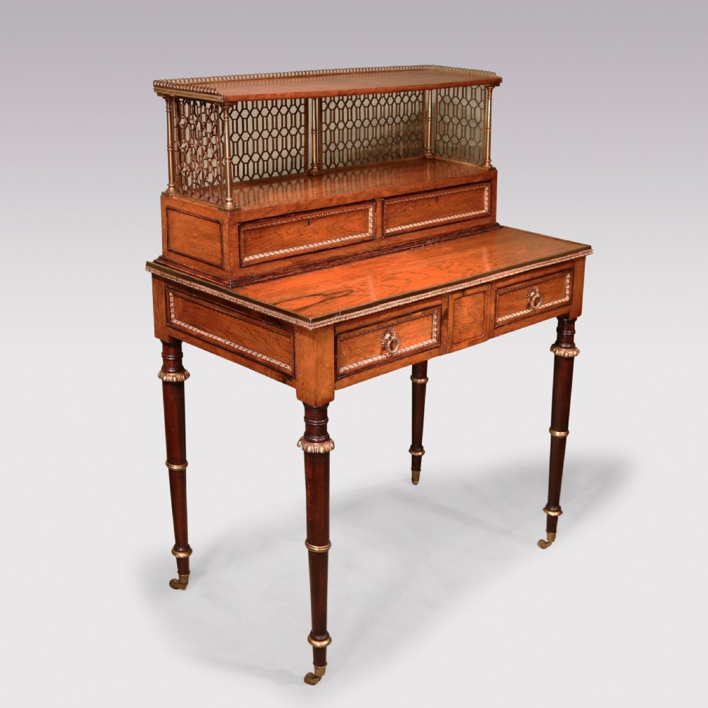 An early nineteenth-century rosewood bonheur du jour writing desk featuring a pierced brass gallery top, small drawers, brass mounts, and turned legs with castors.
