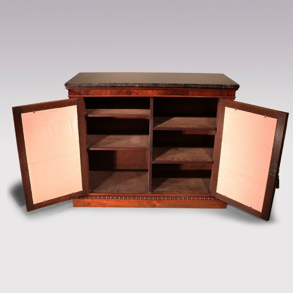 An antique William IV rosewood chiffonier featuring a dark marble top, two brass wire grille doors with pleated fabric backing, and flanking carved side columns. View IV