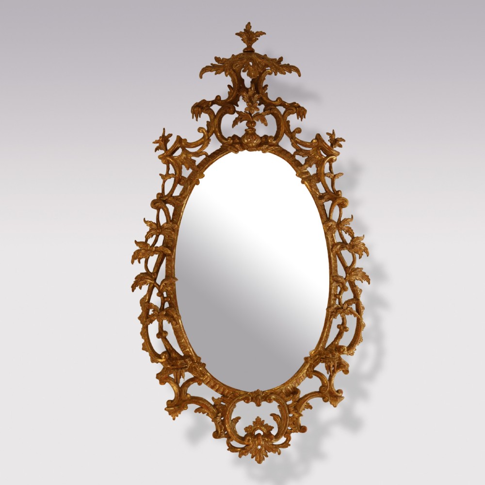 An oval Chippendale period wall mirror featuring a carved and pierced giltwood frame decorated with scrollwork and foliage cresting.
