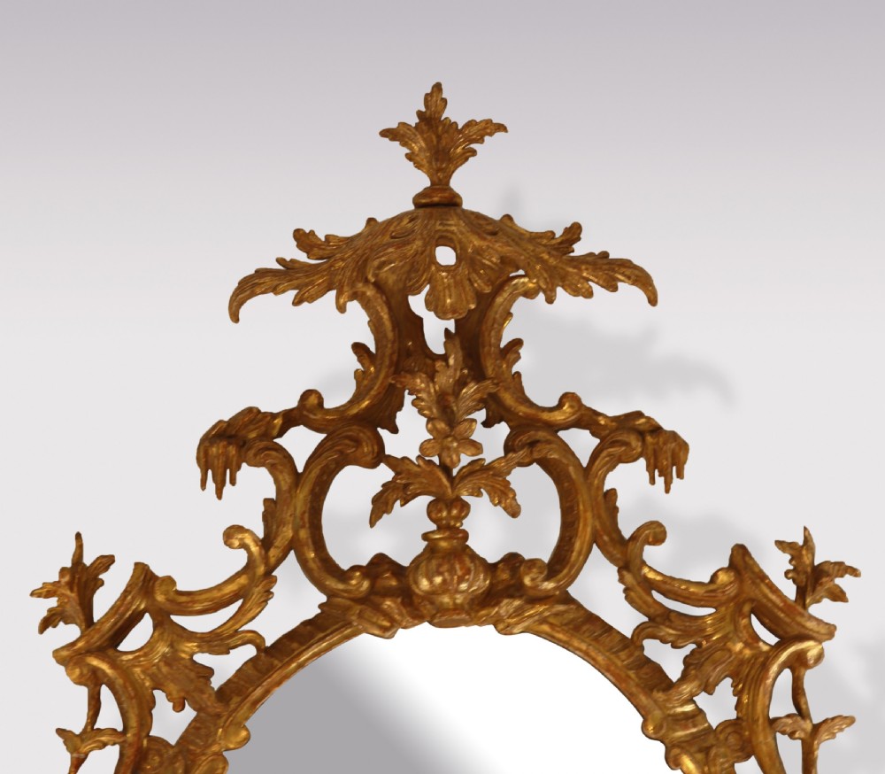 An oval Chippendale period wall mirror featuring a carved and pierced giltwood frame decorated with scrollwork and foliage cresting. View II
