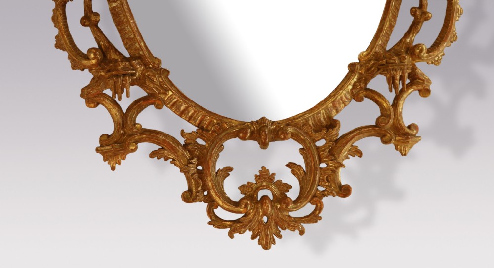 An oval Chippendale period wall mirror featuring a carved and pierced giltwood frame decorated with scrollwork and foliage cresting. View III