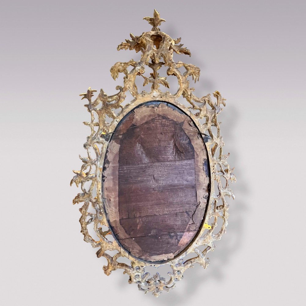 An oval Chippendale period wall mirror featuring a carved and pierced giltwood frame decorated with scrollwork and foliage cresting. View IV