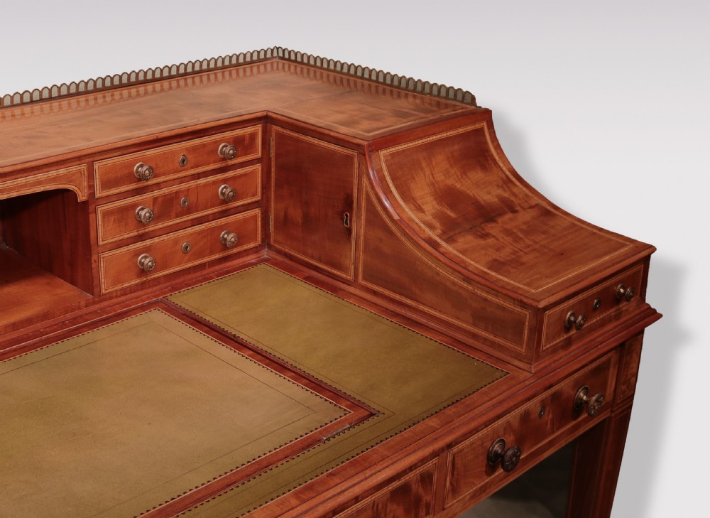 A George III mahogany Carlton House writing desk featuring a U-shaped tiered gallery with drawers, a leather writing top, and tapered legs on castors. View VI