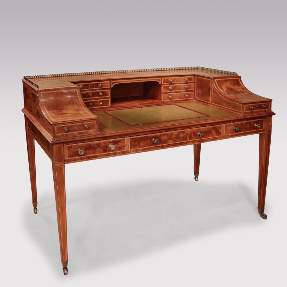 A George III mahogany Carlton House writing desk featuring a U-shaped tiered gallery with drawers, a leather writing top, and tapered legs on castors. View X
