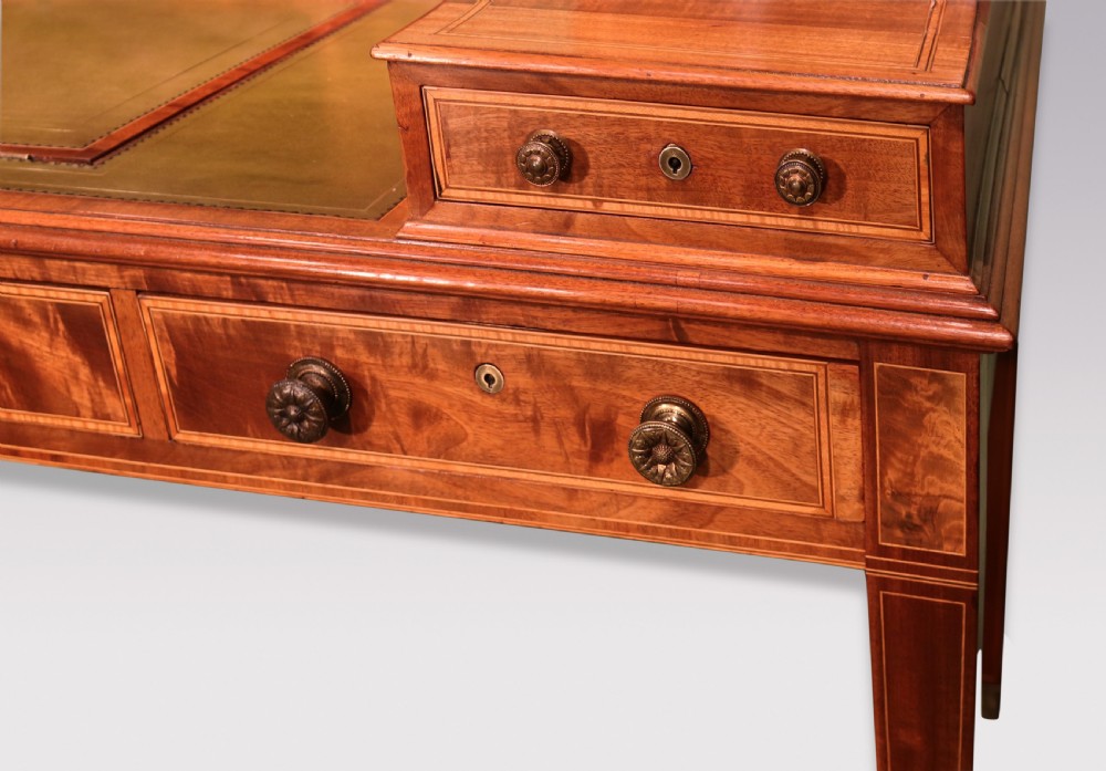 A George III mahogany Carlton House writing desk featuring a U-shaped tiered gallery with drawers, a leather writing top, and tapered legs on castors. View XV