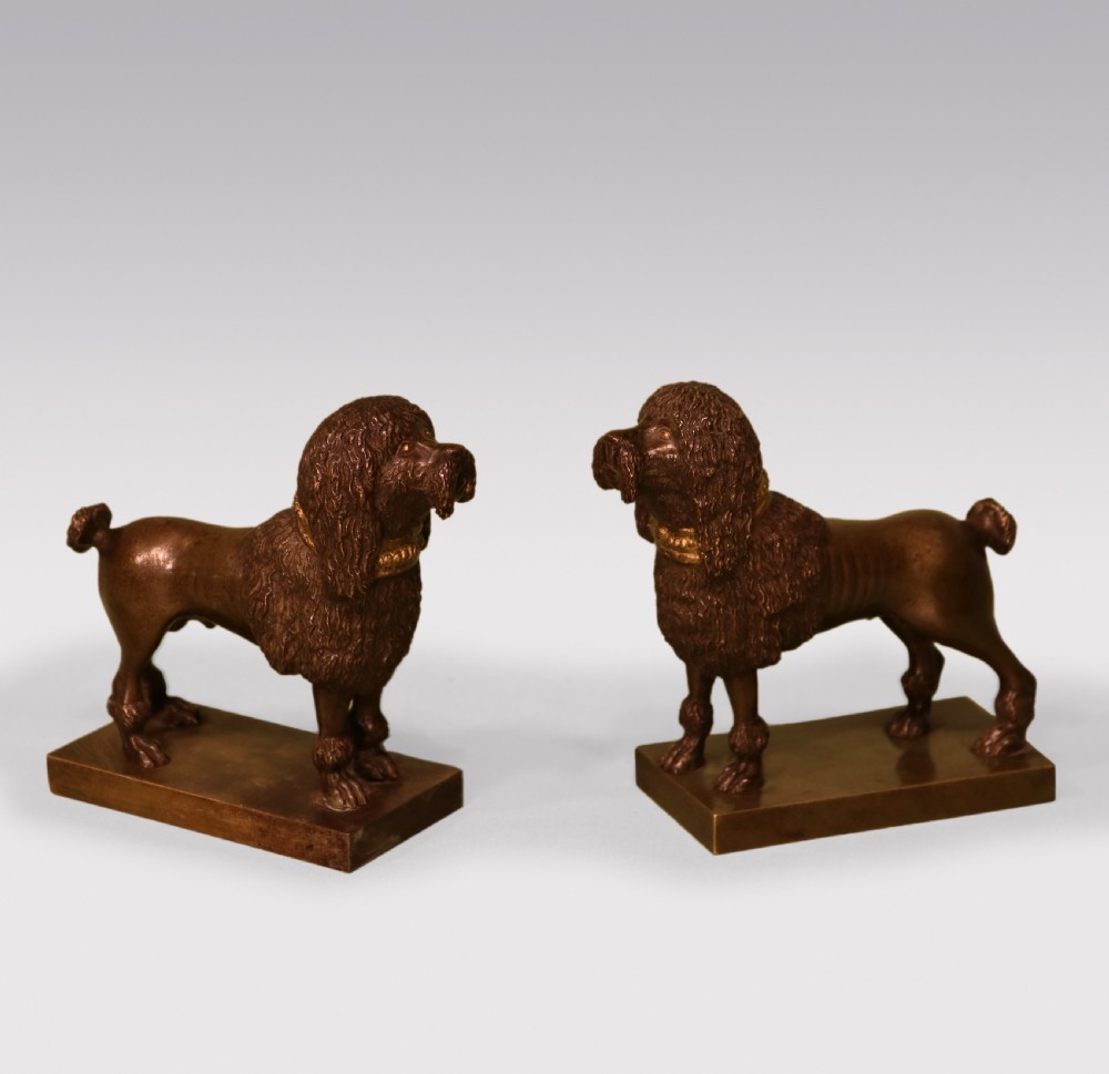 A pair of early 19th-century dark brown bronze poodle figures featuring gilded collars standing on rectangular bases.