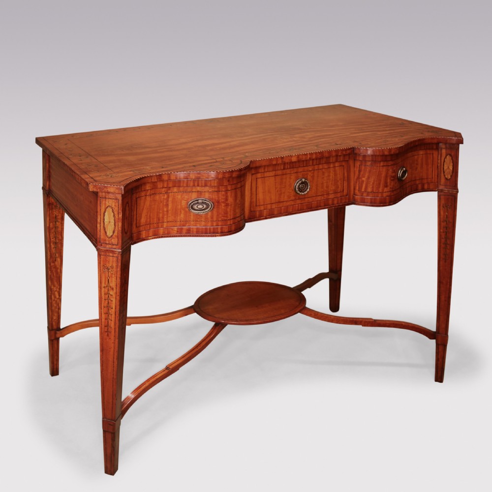 A late 19th-century satinwood hall table featuring a serpentine front, three drawers with brass handles, floral marquetry inlay on square tapered legs, and a central circular under-shelf connected by curved stretchers.