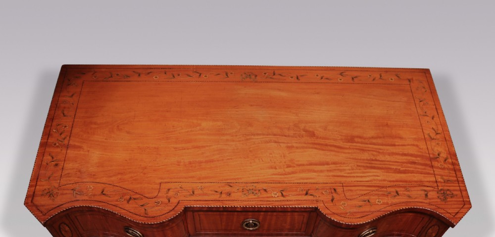 A late 19th-century satinwood hall table featuring a serpentine front, three drawers with brass handles, floral marquetry inlay on square tapered legs, and a central circular under-shelf connected by curved stretchers. View III