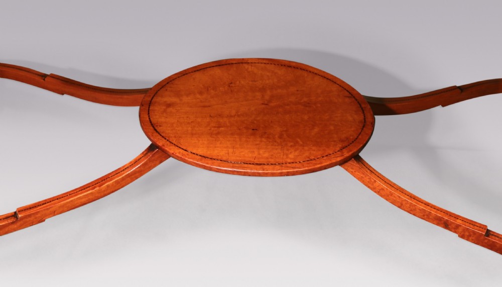 A late 19th-century satinwood hall table featuring a serpentine front, three drawers with brass handles, floral marquetry inlay on square tapered legs, and a central circular under-shelf connected by curved stretchers. View VII