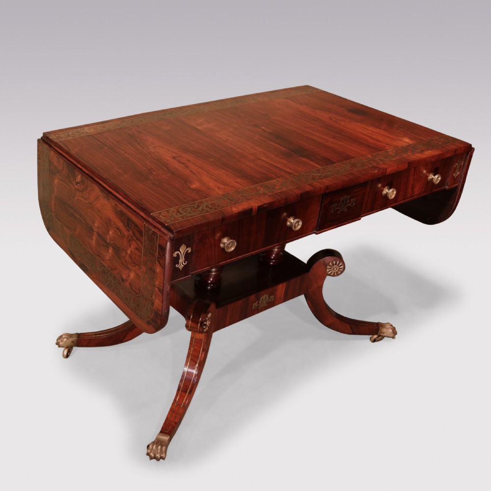 An antique Regency rosewood sofa table with intricate brass inlay, drop-leaf ends, shallow drawers, and swept legs on brass paw castors. View II