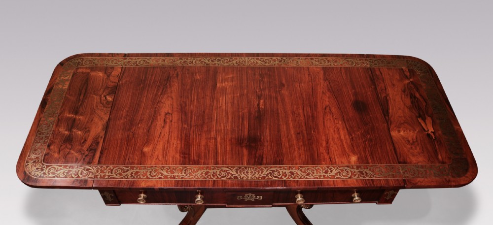 An antique Regency rosewood sofa table with intricate brass inlay, drop-leaf ends, shallow drawers, and swept legs on brass paw castors. View III