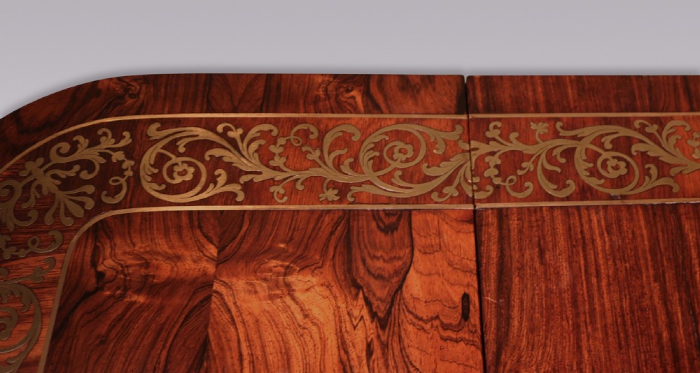 An antique Regency rosewood sofa table with intricate brass inlay, drop-leaf ends, shallow drawers, and swept legs on brass paw castors. View IV