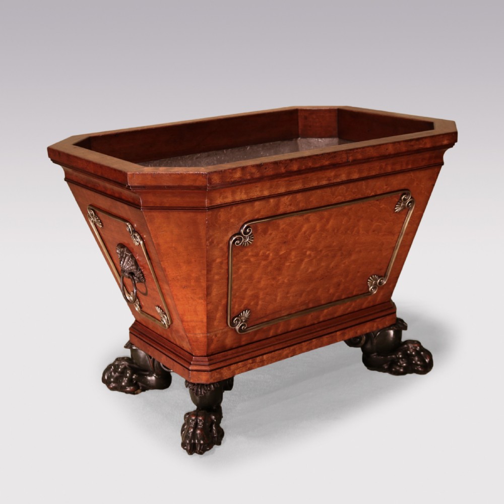A Regency mahogany cellarette featuring tapered sides, brass inlay, brass lion mask handles, and carved claw feet.